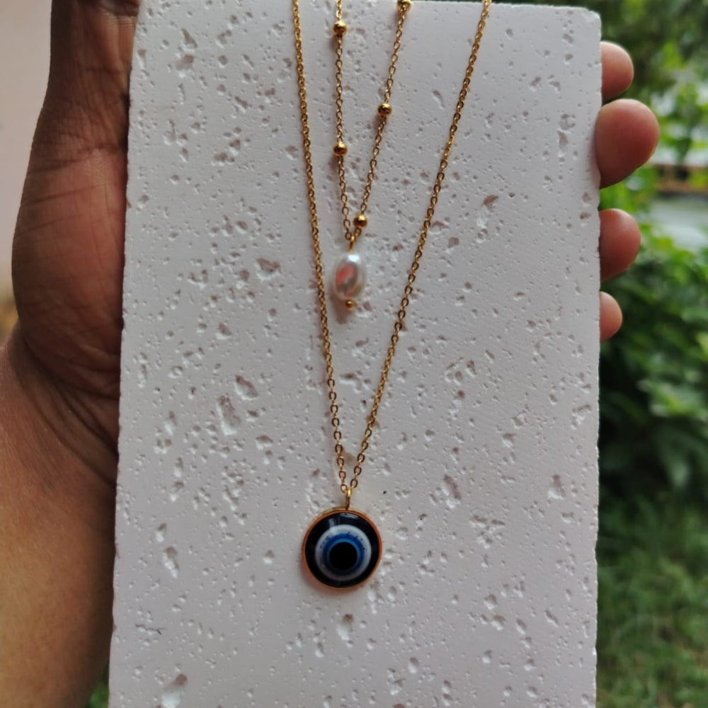 Golden Evil Eye Necklace on a textured White Board Held By a Hand