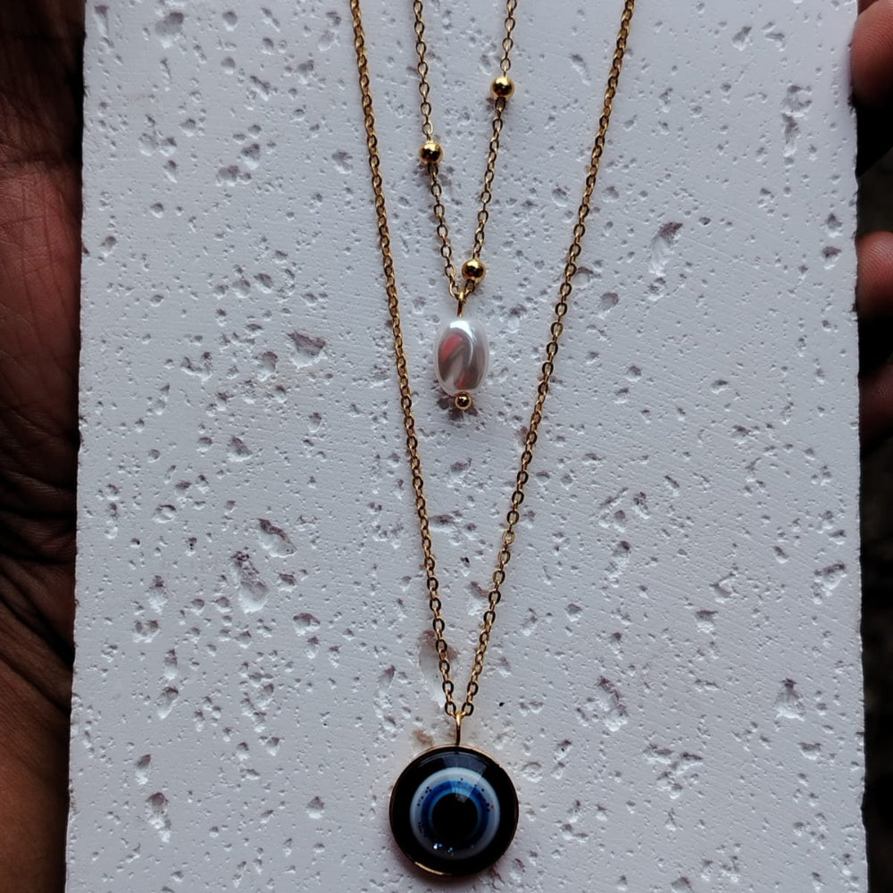 Golden Double-layer Evil Eye Necklace with Pearl on a textured white background