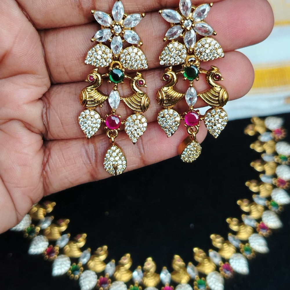 Decorative gold earrings with gemstones held in a hand, necklace in the background
