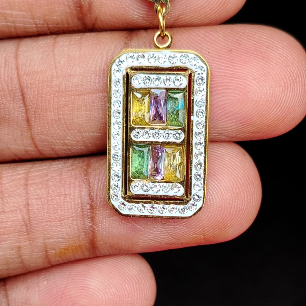 Golden pendant with colorful gemstones held between fingers against a dark background