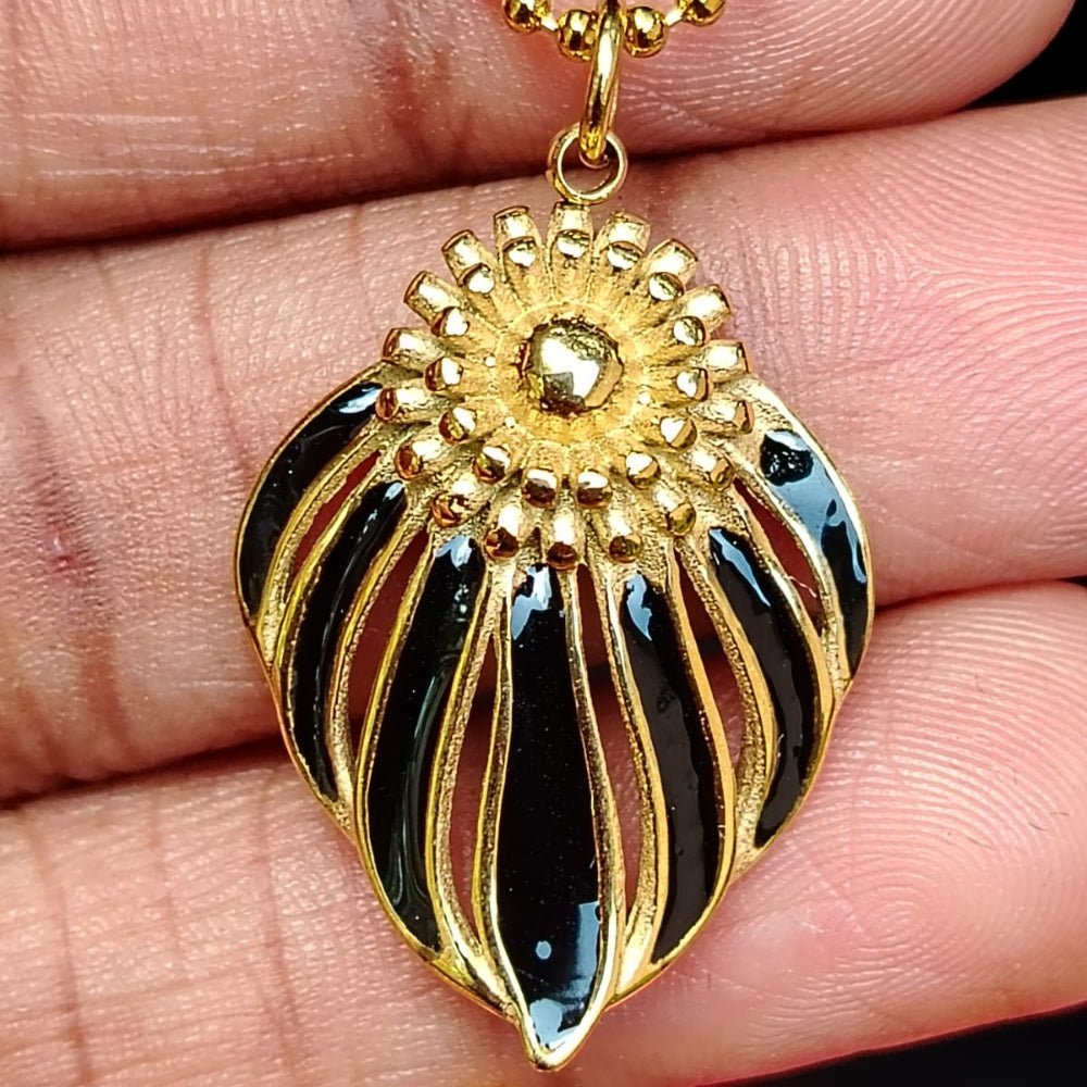 Gold and black pendant held between fingers with a blurred red background