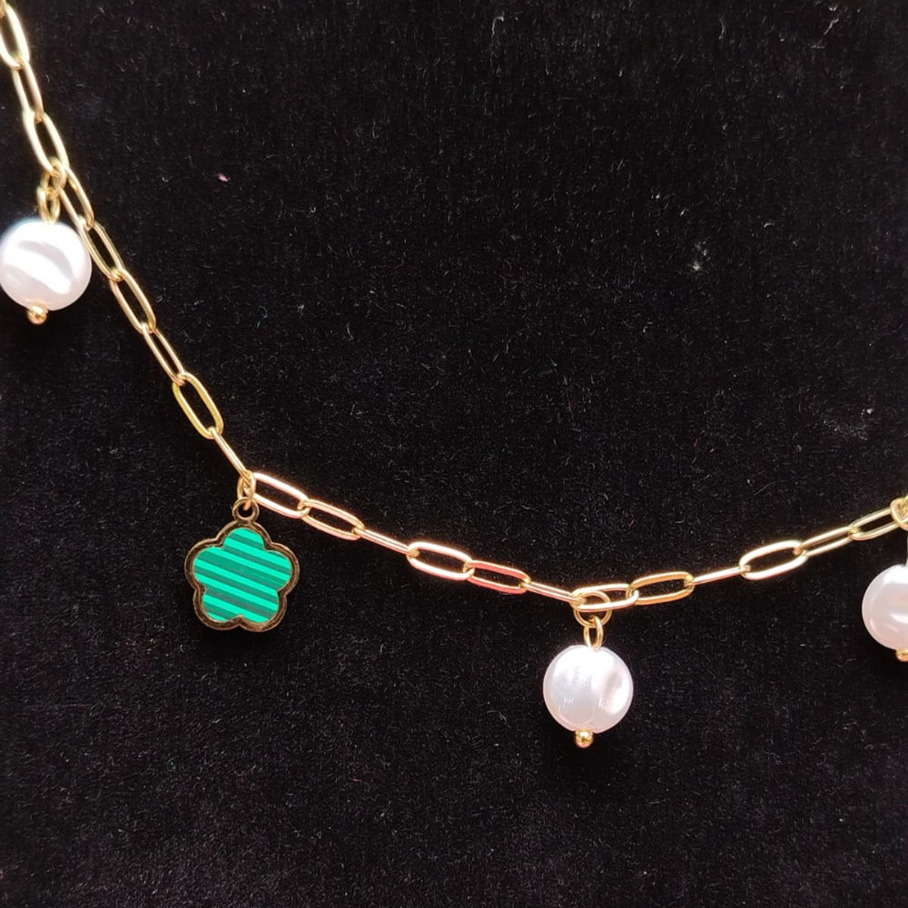 Necklace with gold chain, green clover charm, and pearl beads on a black background