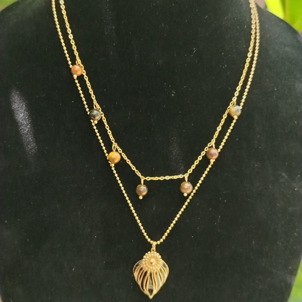 Gold necklace with leaf pendant on a black mannequin bust with green foliage in the background
