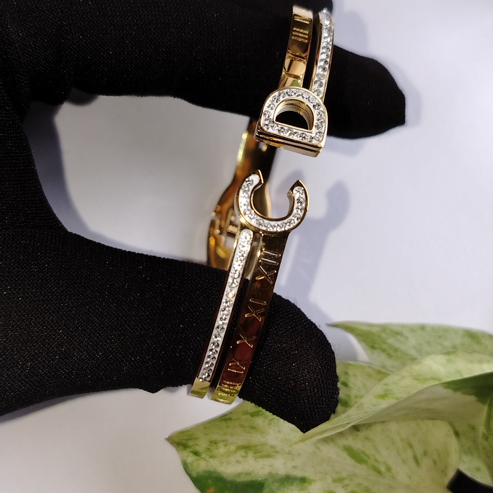 Brand-inspired golden bracelet with Roman Numerals Imprints design, held by a gloved hand on a white background.
