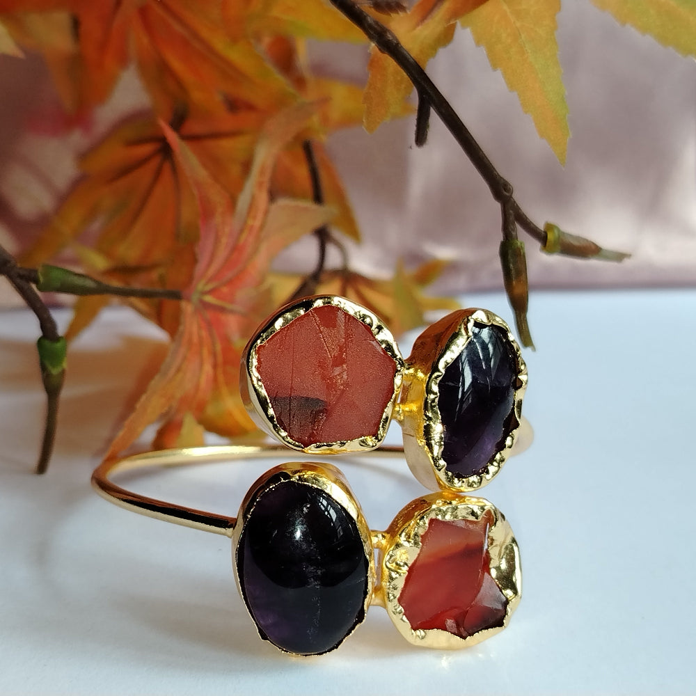Golden Bracelet with Carnelian and Amethyst Stones on a White Surface with Autumn Leaves in the Background