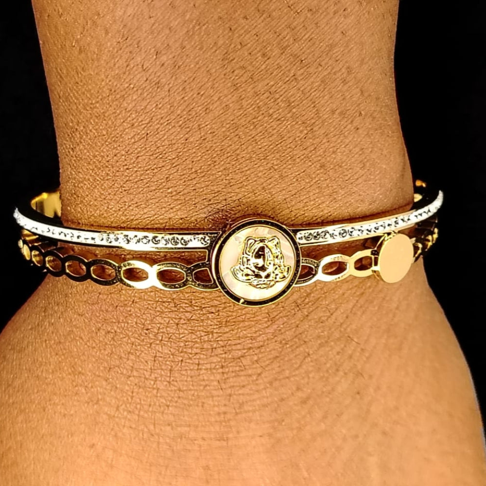 Gold bracelet with a circular emblem on a wrist against a black background