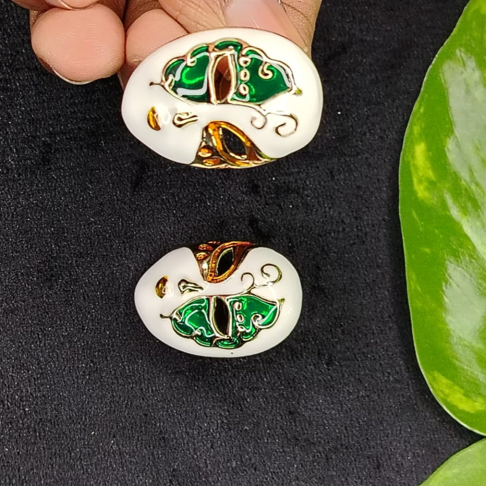 Model Holding Pair of Mask-Shaped Earrings with Green, Red, and Gold Design on a Black surface.