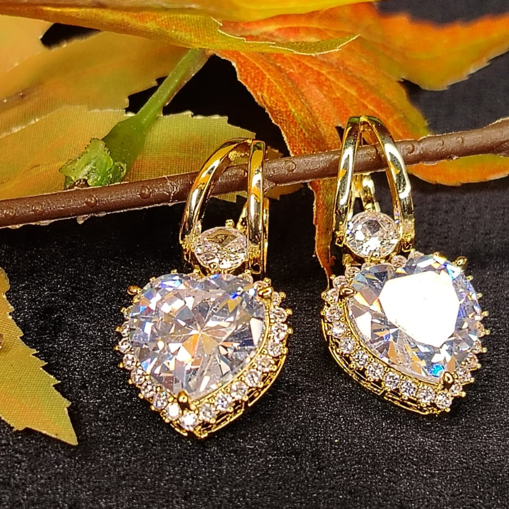 Golden heart-shaped American Diamond Drop Hoops earrings on a Dark Surface with Leaves.