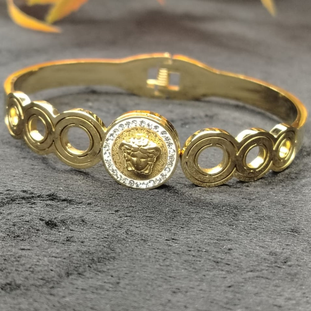 Golden Bracelet with Circular Design and Logo on a Textured Surface