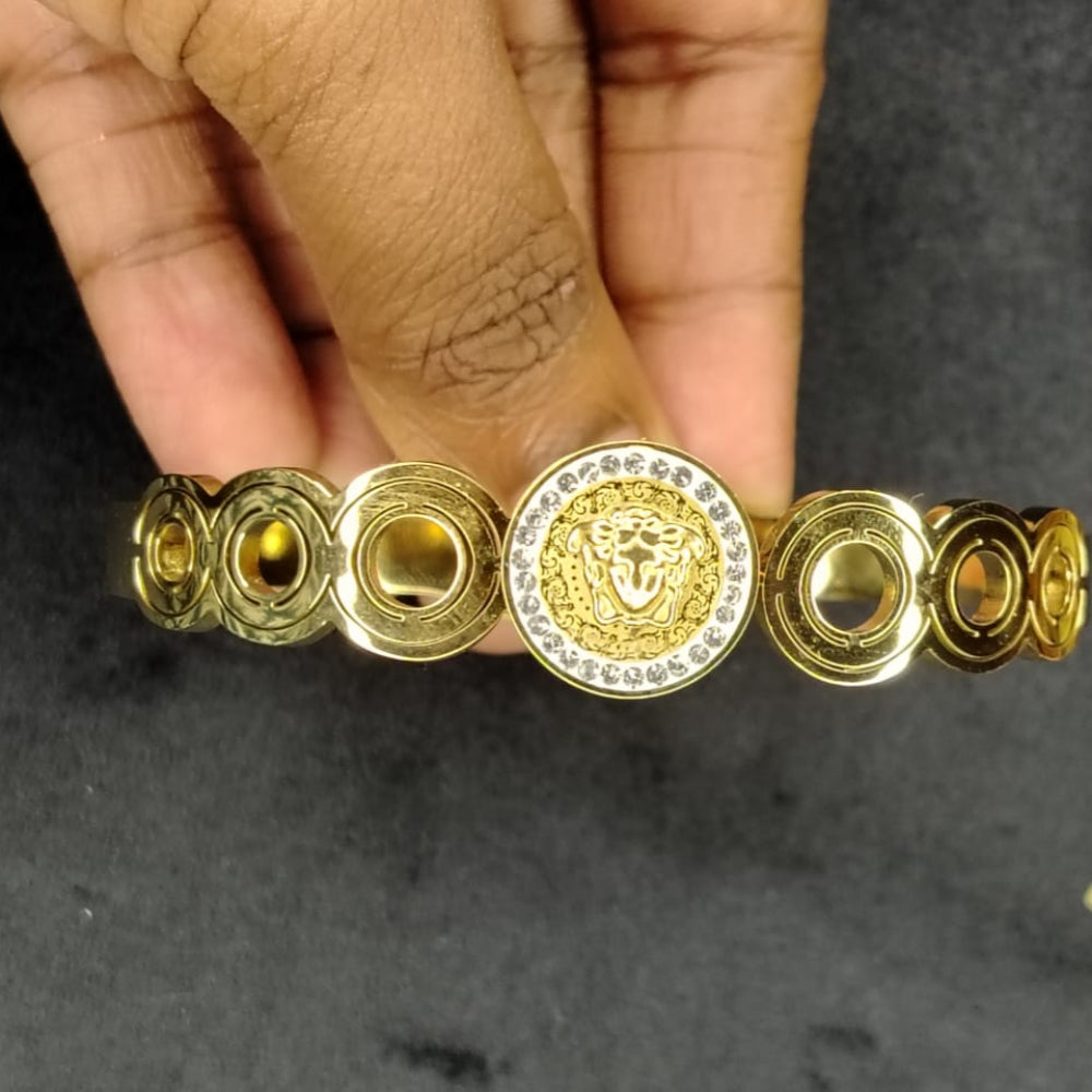 Golden Bracelet with a Brand Logo in the Centre held by a Hand on a Dark Background