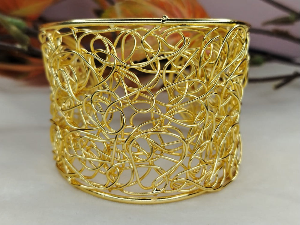 Gold Plated Broad Filigree Bracelet against a Blurred Background