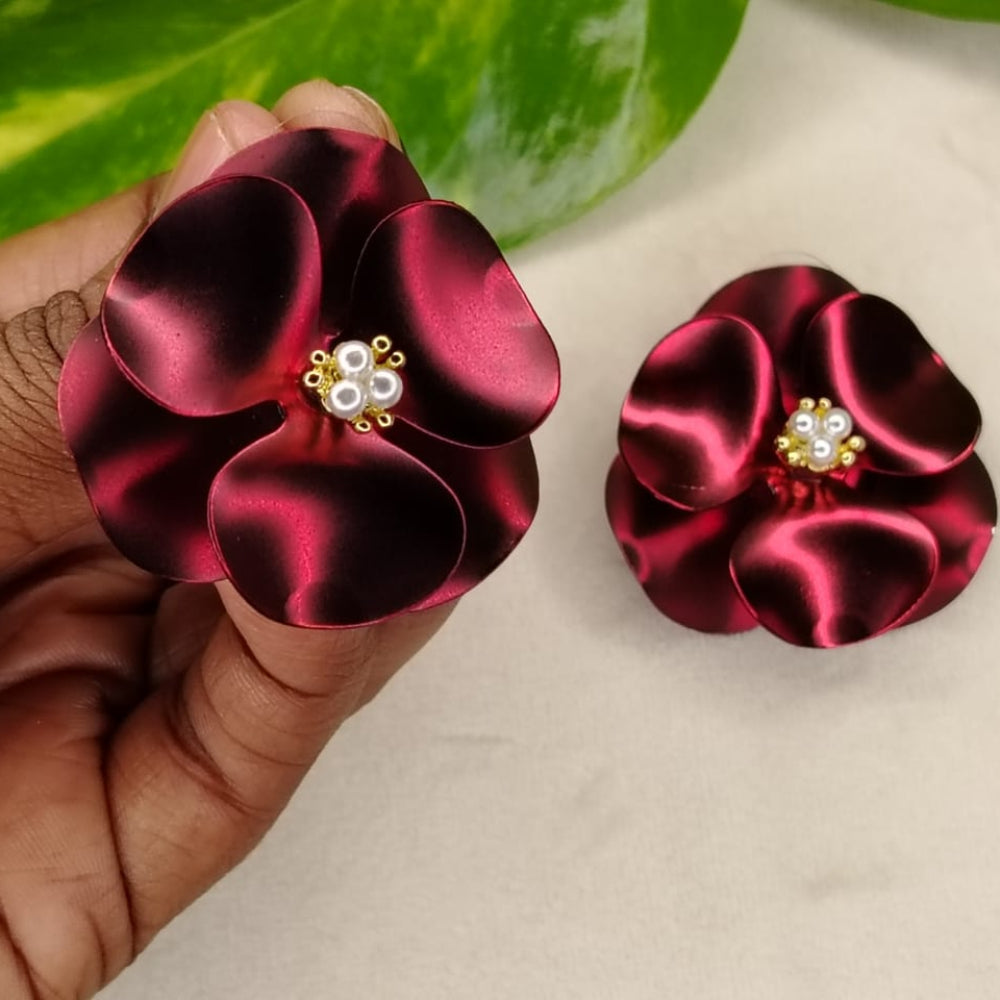 Pearl Centred Broad Petal Maroon Earrings Held by Hands angainst White Background and Leaves
