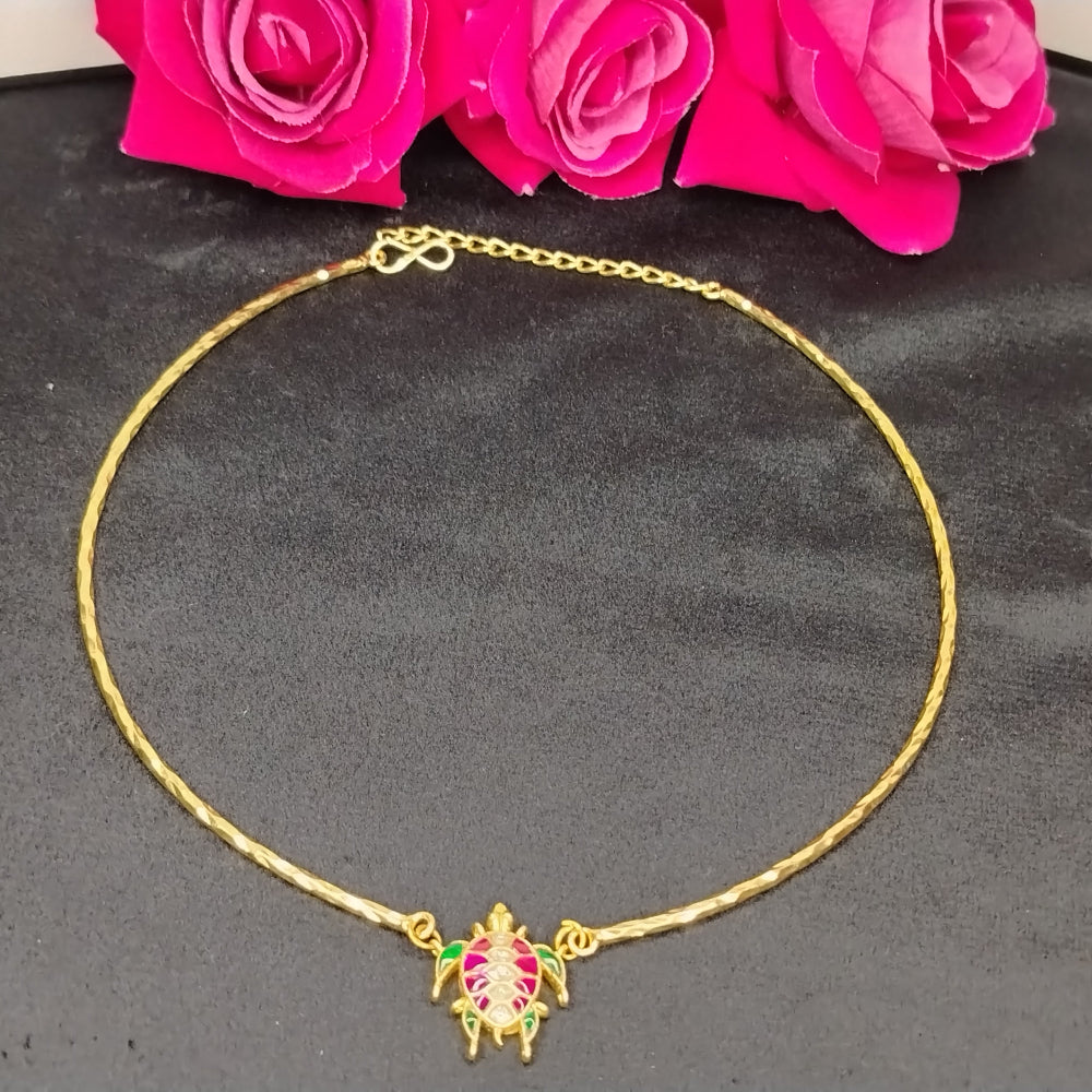 Gold necklace with a turtle pendant on a dark surface with pink flowers in the background