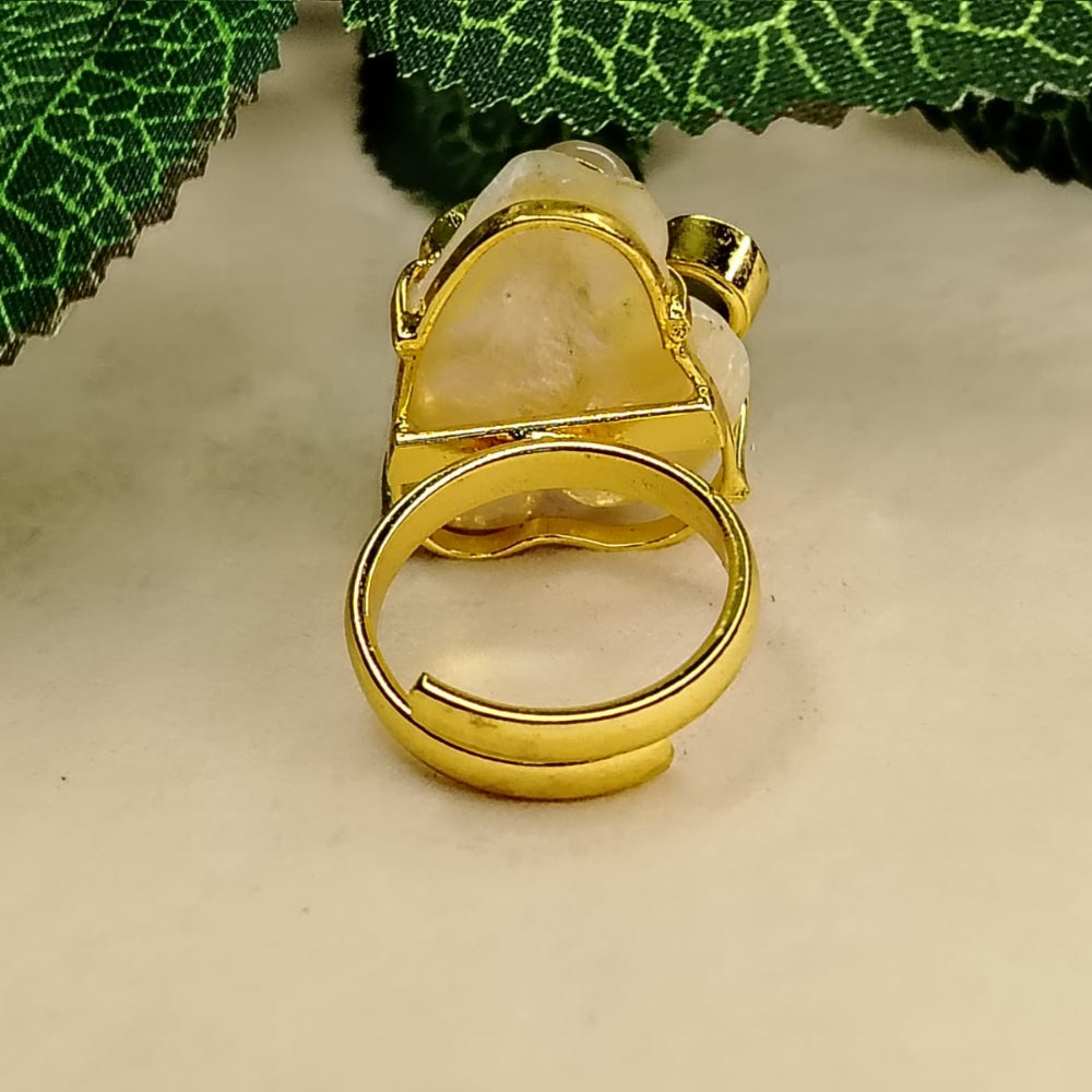 Back View of Golden Pearl Ring on Beige Surface Against Green Leaves