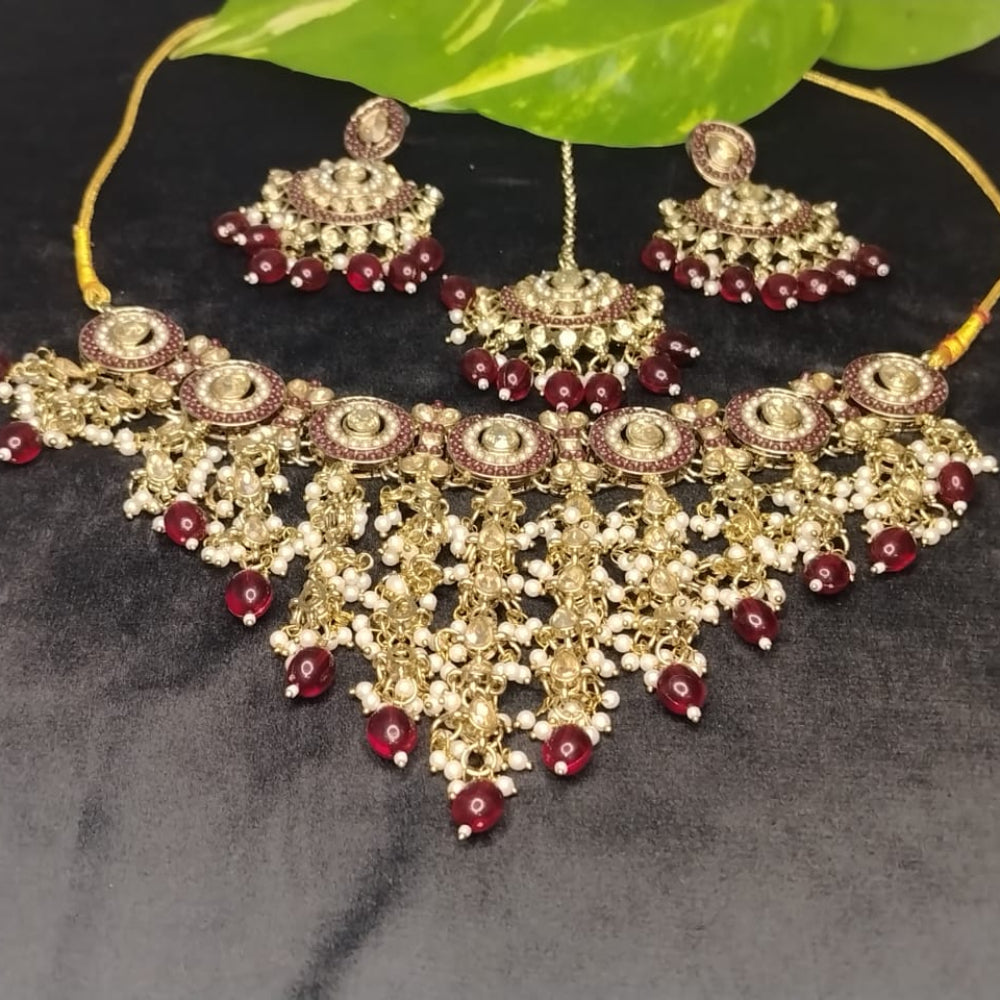Golden Ornate Jewellery Set with Maroon Beads and Kundan on a Black Surface