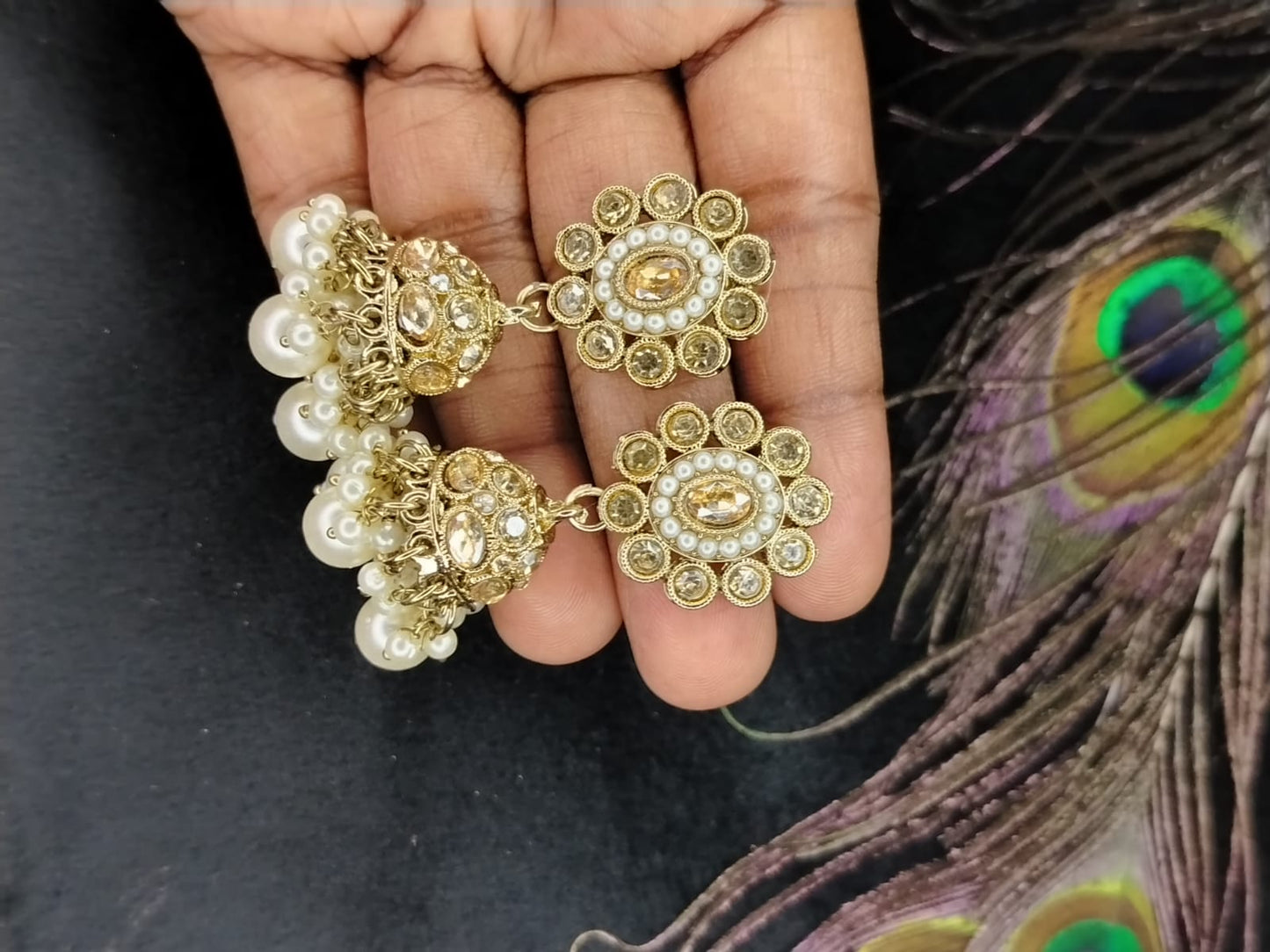 Kundan Jhumkas with Pearl Beads Held by Hands on a Black Surface against Peacock Feather
