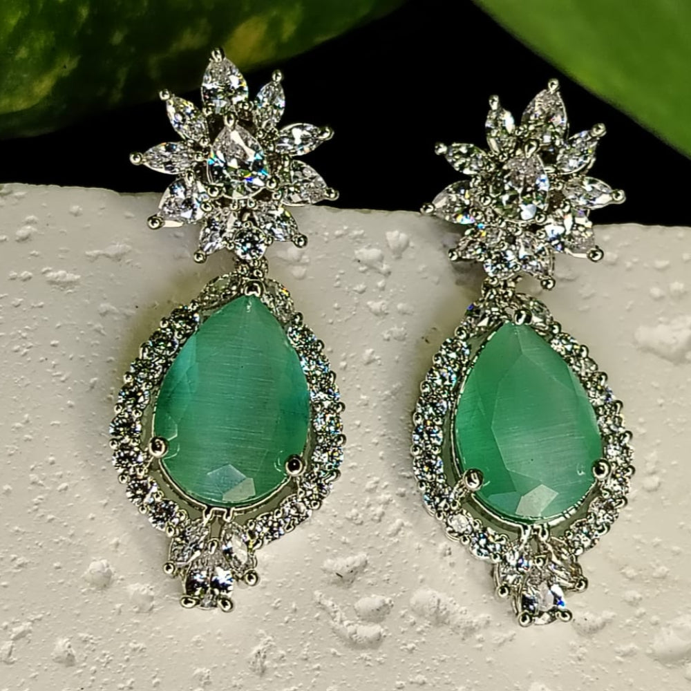 Pair of earrings with green teardrop stones and starburst designs on a textured surface.