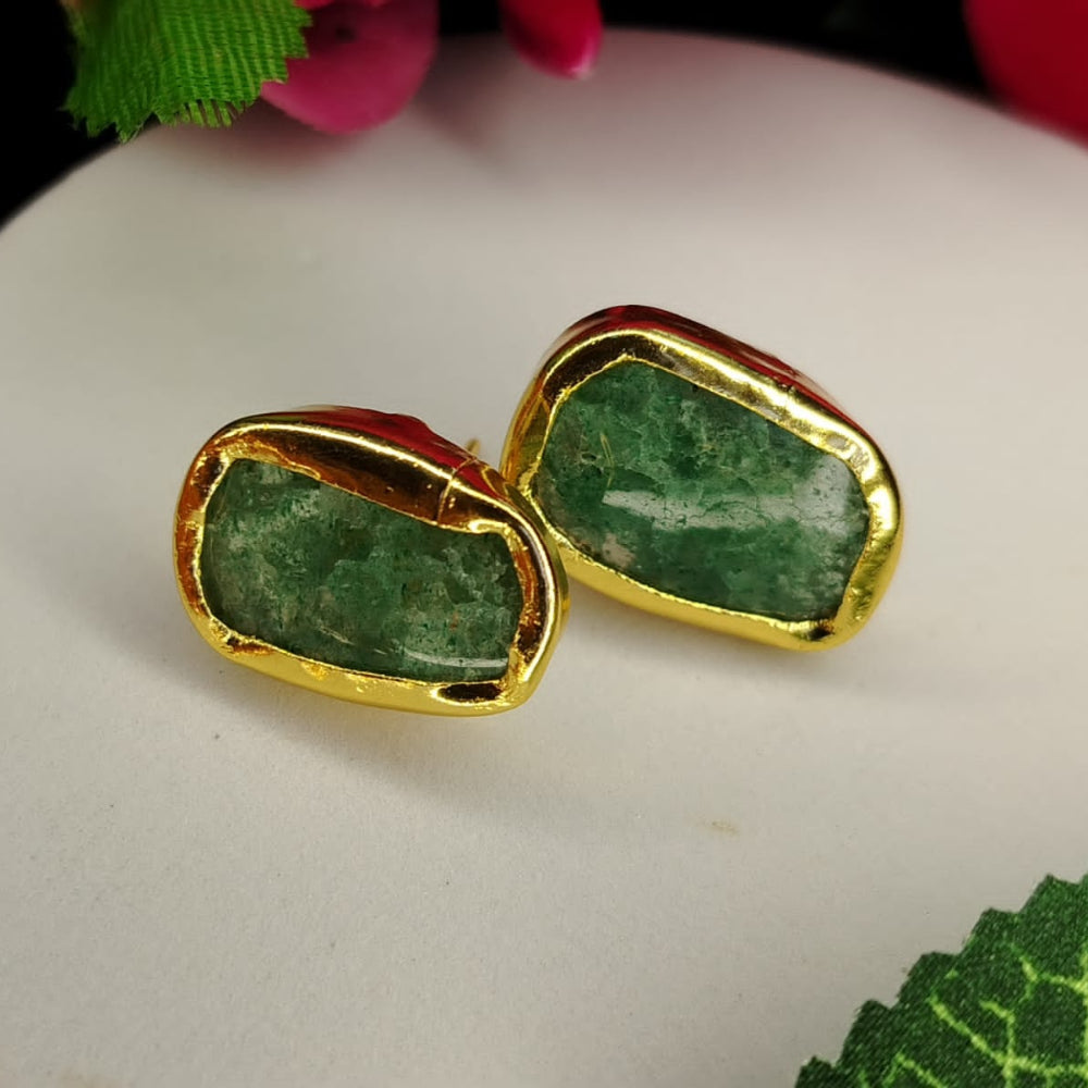Gold-framed green gemstone earrings on a white surface with floral background