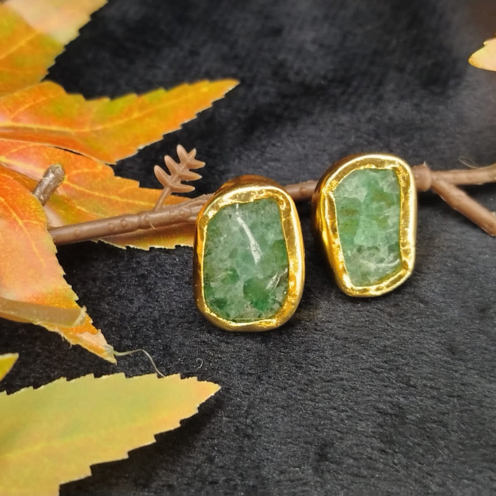 Gold-framed green stone earrings on a dark surface with autumn leaves.