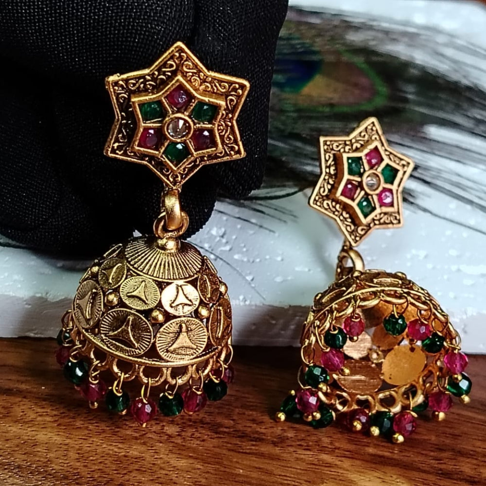 Golden Jhumka with colorful stones on a wooden surface with a peacock feather