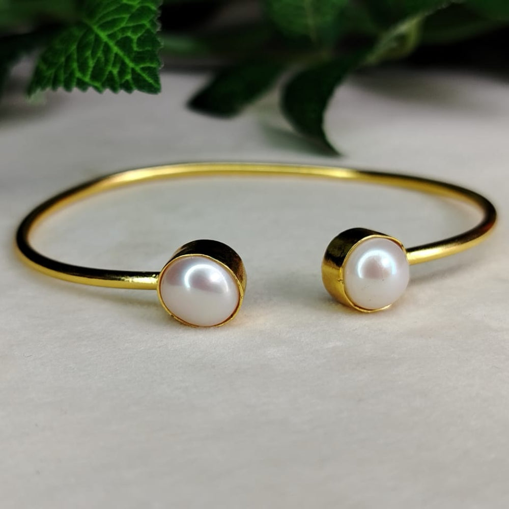 Golden bracelet with pearls on a light background and Green leaves