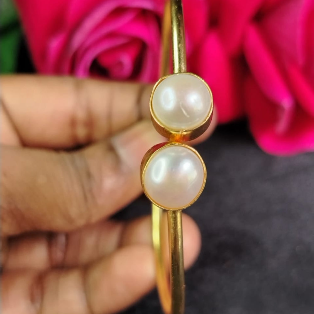 Golden bangle with pearls held by a hand against a pink rose background