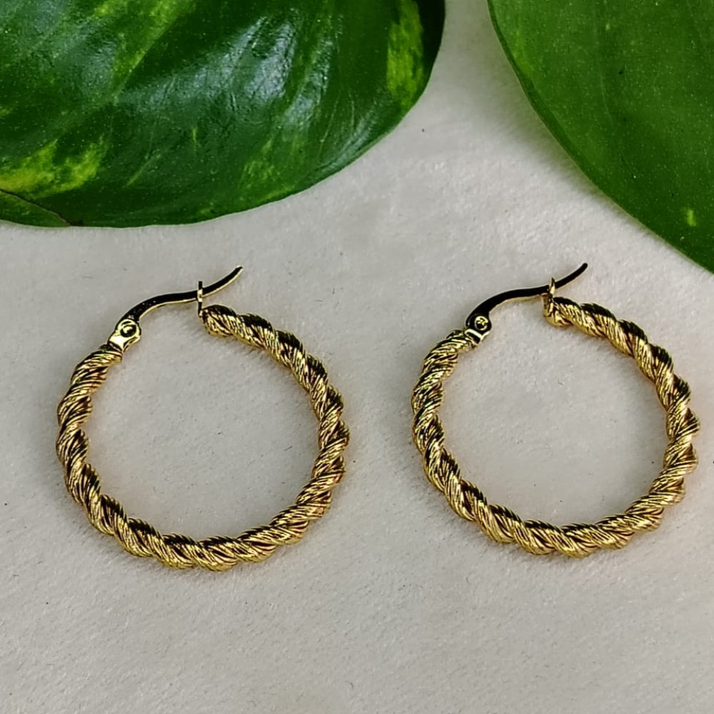 Golden hoop earrings on a light surface with green leaves in the background