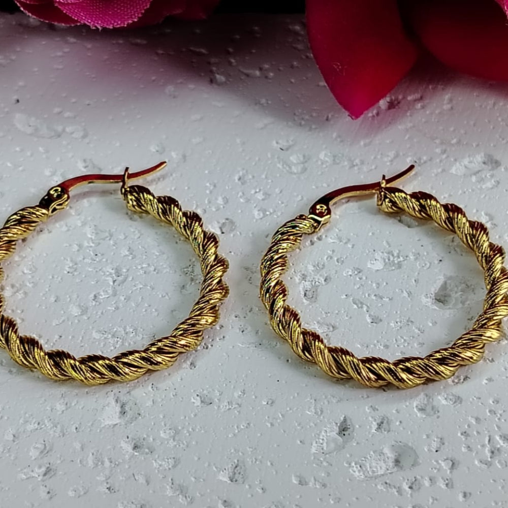 Gold hoop earrings on a textured white surface with pink flowers in the background