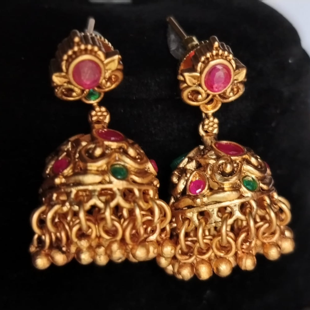 Golden Jhumka earrings with red and green stones on a black background