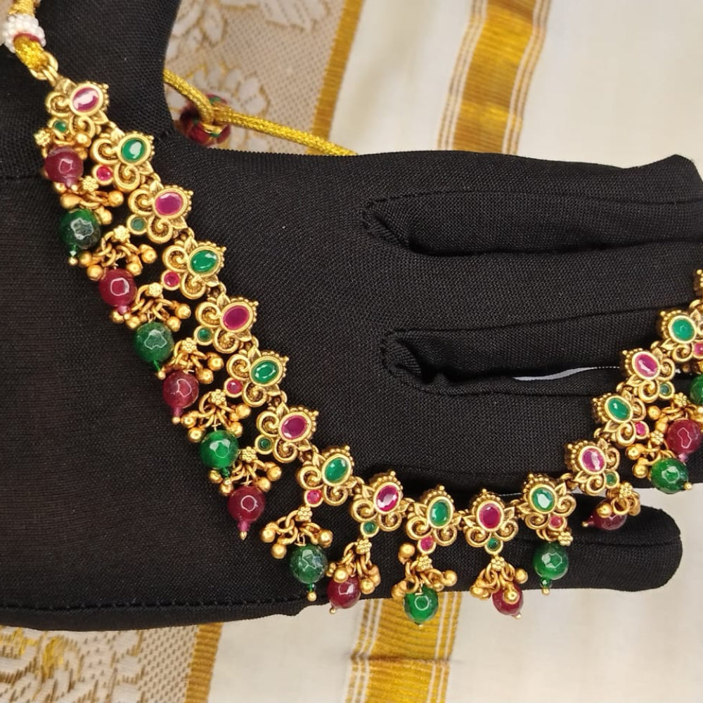 Golden necklace with red and green gemstones held by a gloved hand against a neutral background