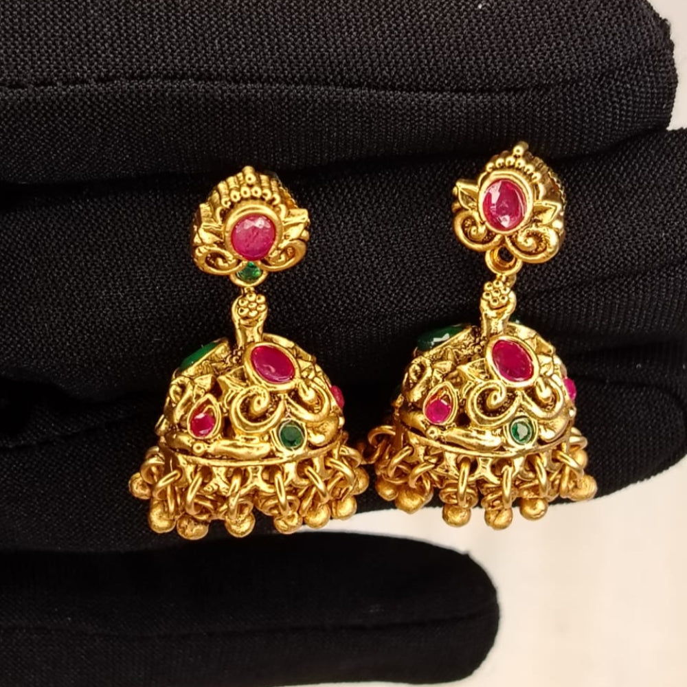 Golden earrings with red and green gemstones on a black glove