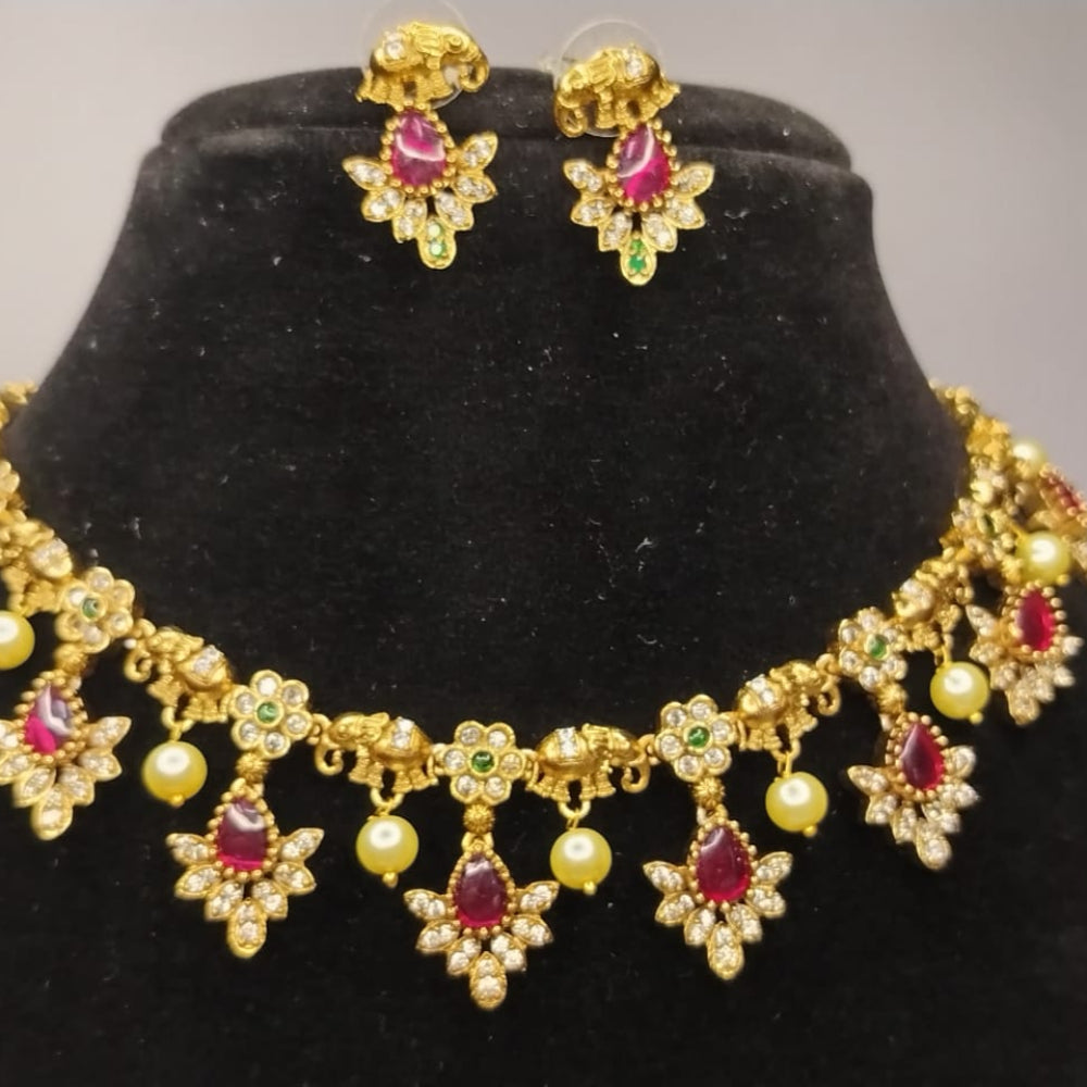 Golden necklace and earrings with red and green gemstones on a black mannequin bust.