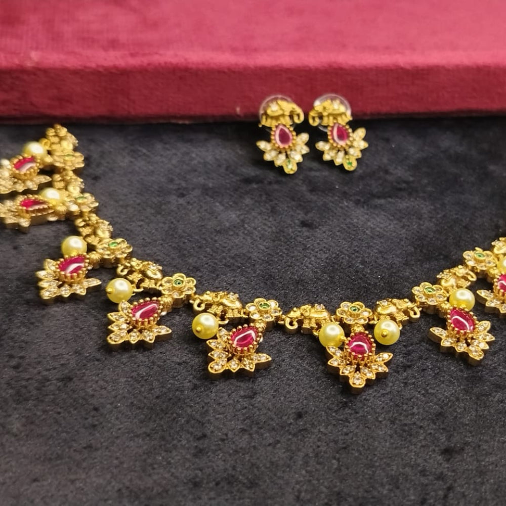 Gold necklace with red gemstones and matching earrings on a dark surface.