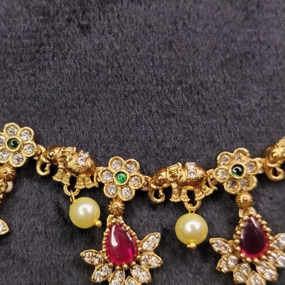 Gold necklace with floral designs, pearls, and red gemstones on a dark background