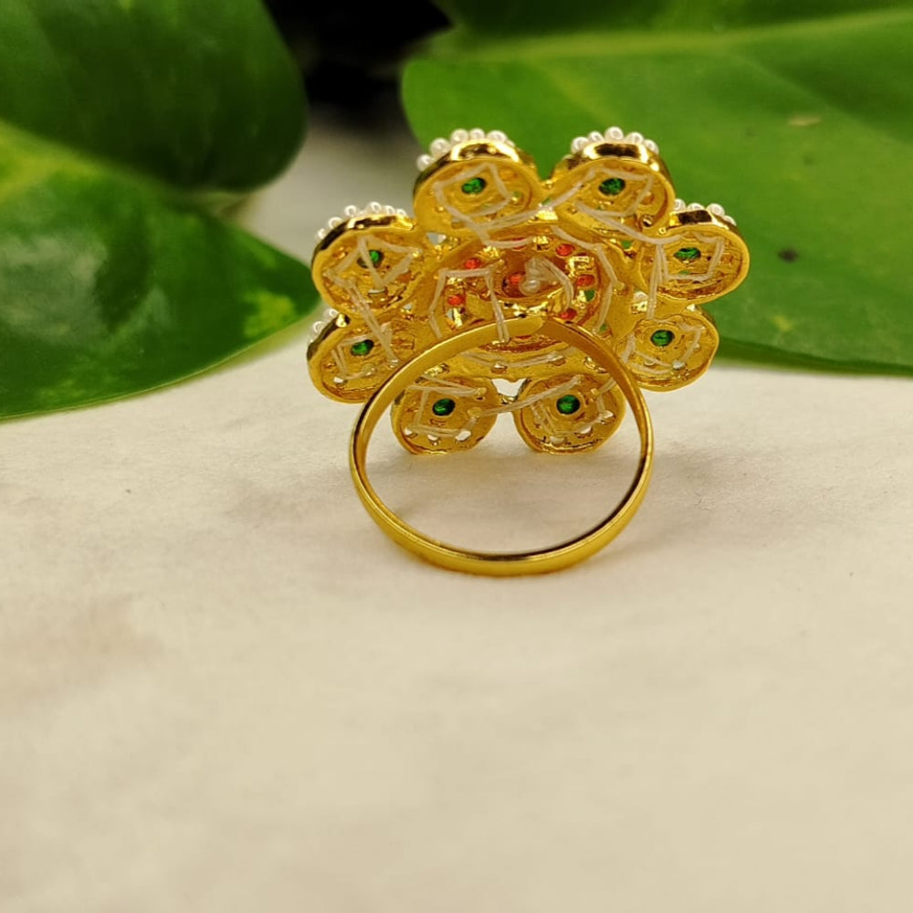 Gold ring with floral design on a beige surface with green leaves in the background