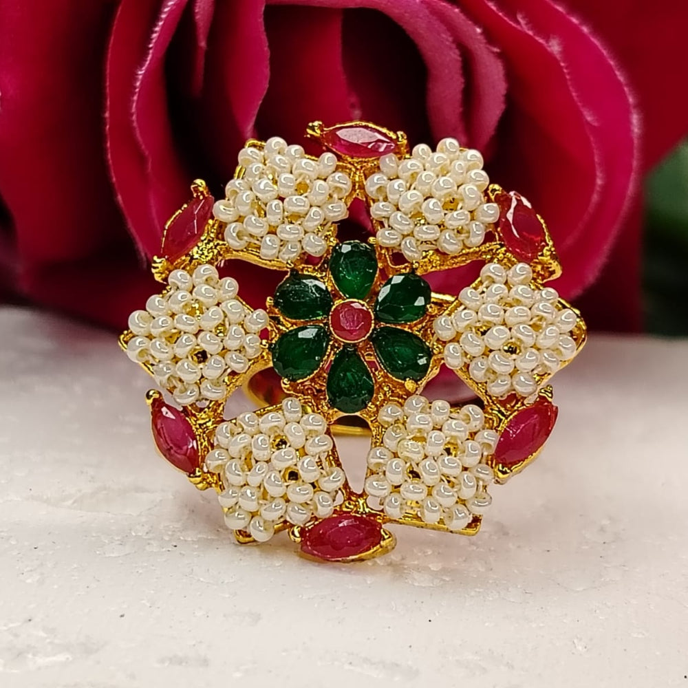 Decorative ring with pearls, red stones, and green gemstones on a white surface with a red rose in the background.