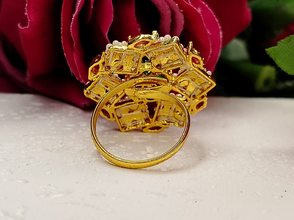 Gold ring with intricate design on a white surface with red flowers in the background