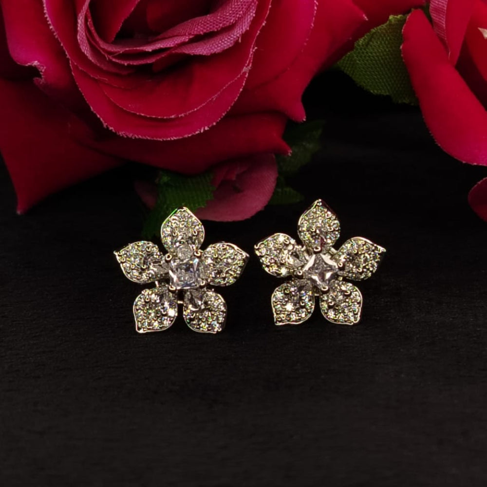 Flower-shaped silver earrings with American Diamonds on a black background with red flowers.