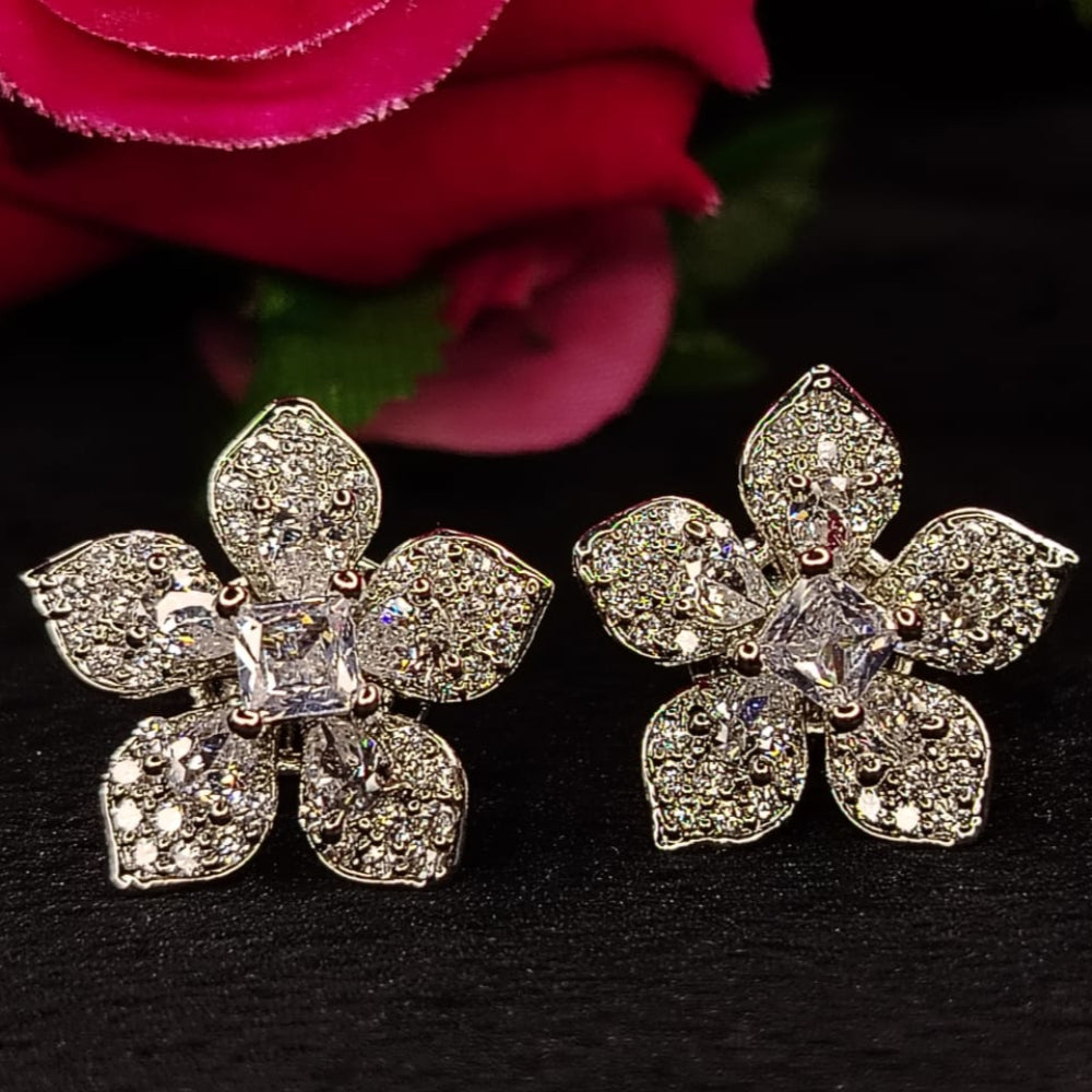 Flower-shaped earrings with American Diamonds on a dark background with red flowers.