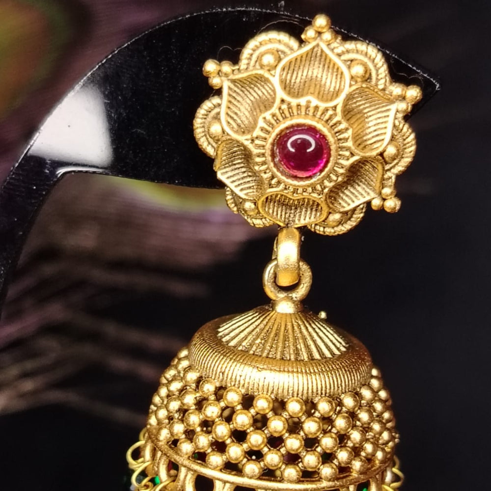 Gold jhumka earring with red and green gemstones on a dark background