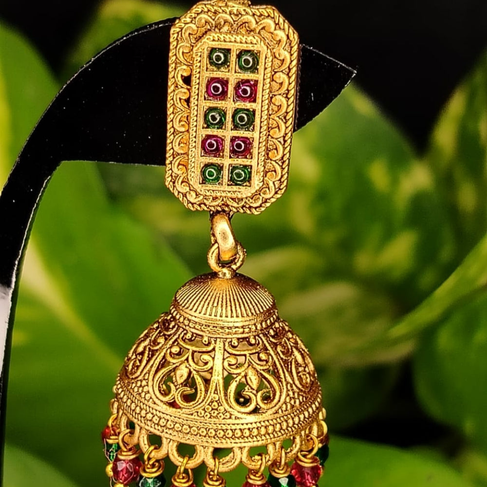 Gold jhumka earring with gemstones on a green leaf background