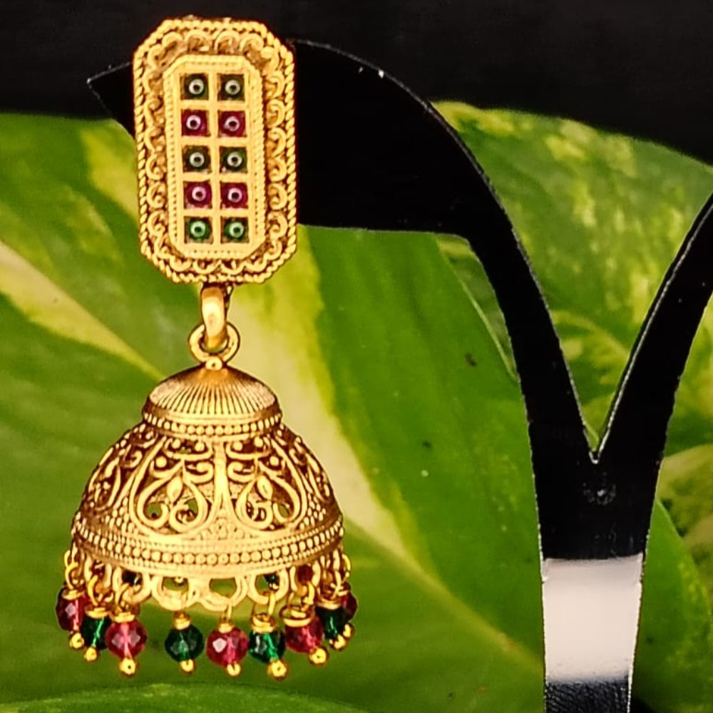 Gold earrings with colorful beads on a black stand against green leaves