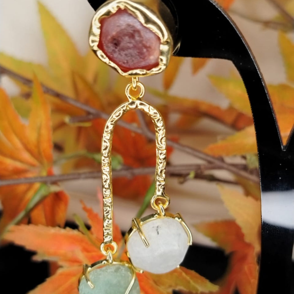 Golden earrings with gemstones on a stand with autumn leaves in the background