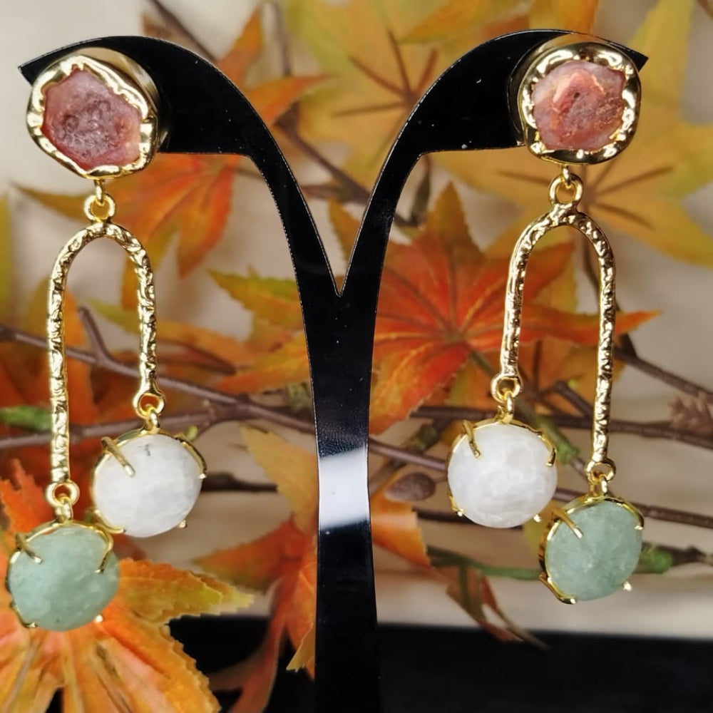 Gold earrings with gemstones on a stand against a nature-themed background