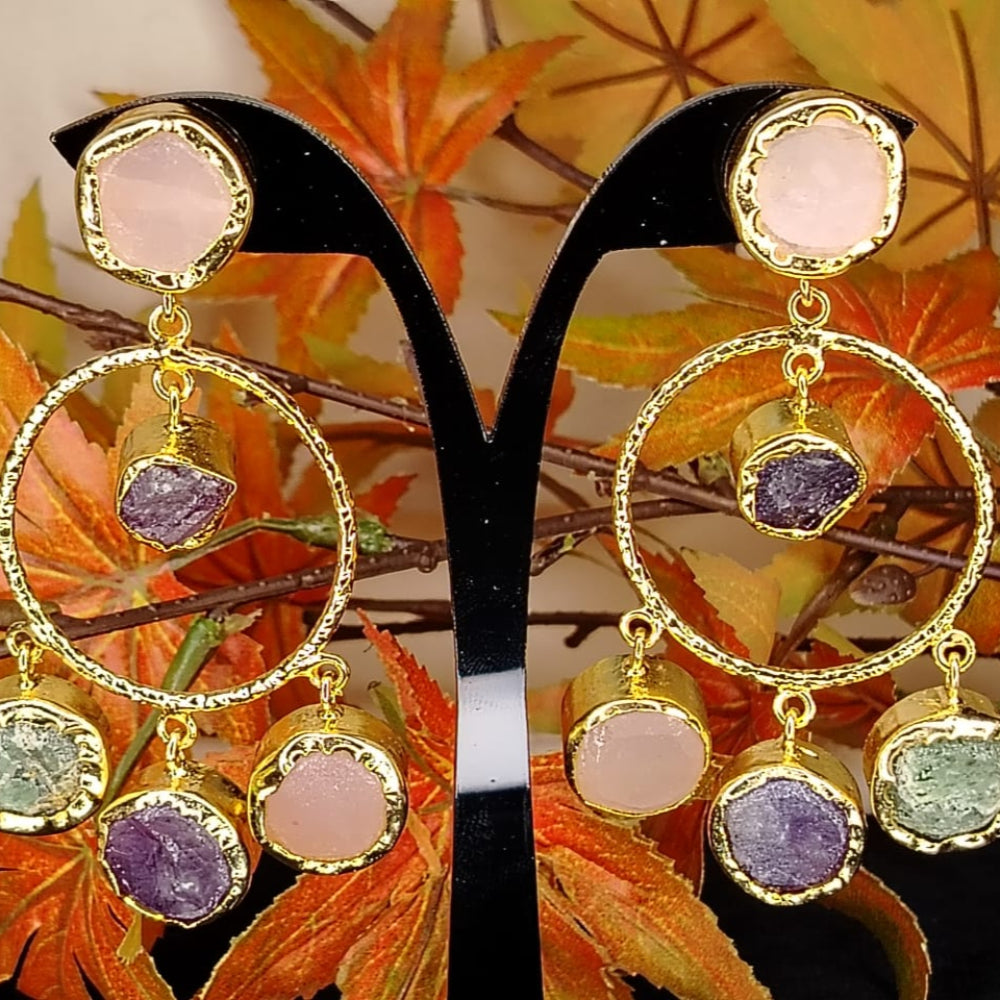 Gold earrings with gemstones on a black stand against an autumn leaf background