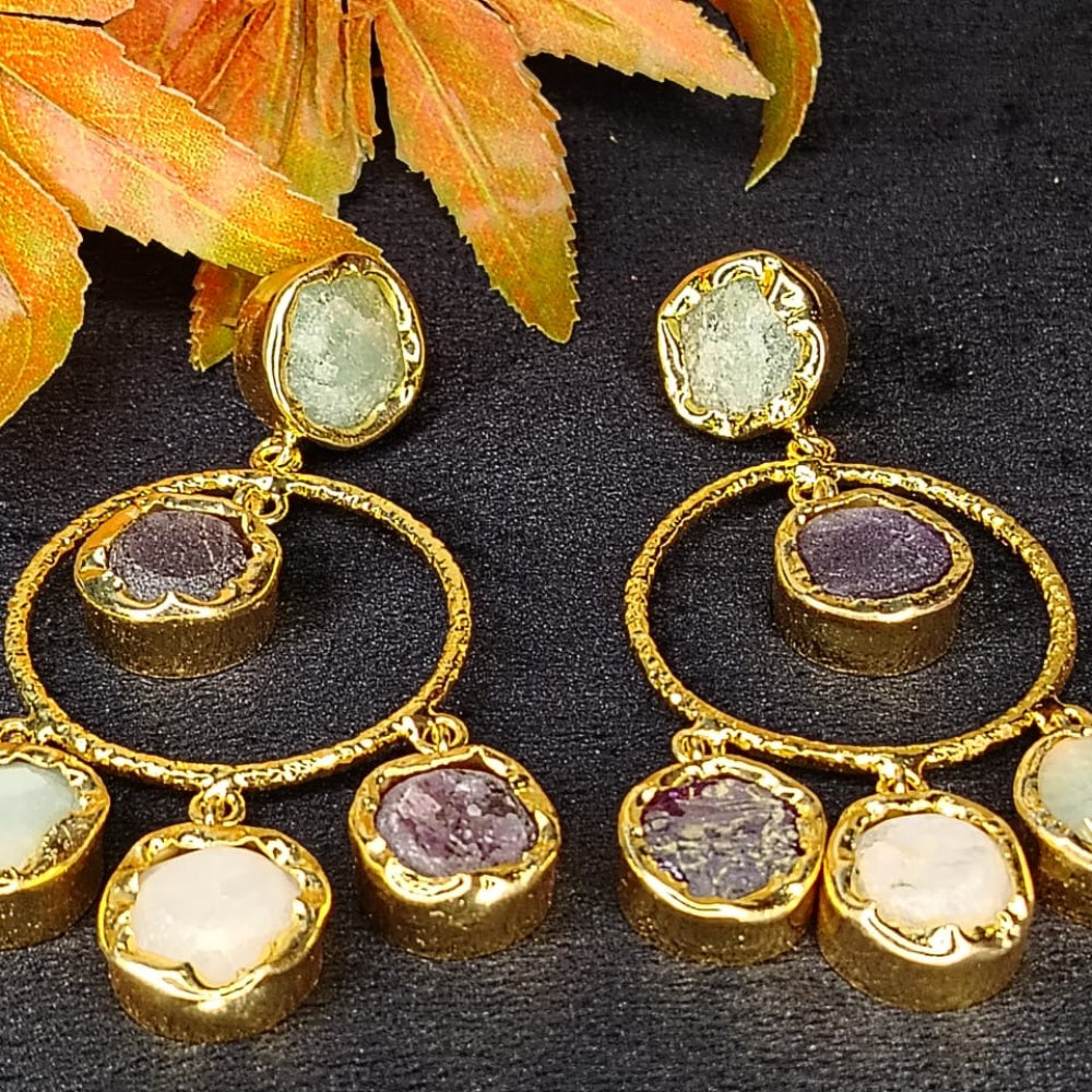 Gold earrings with gemstones on a dark surface with autumn leaves.