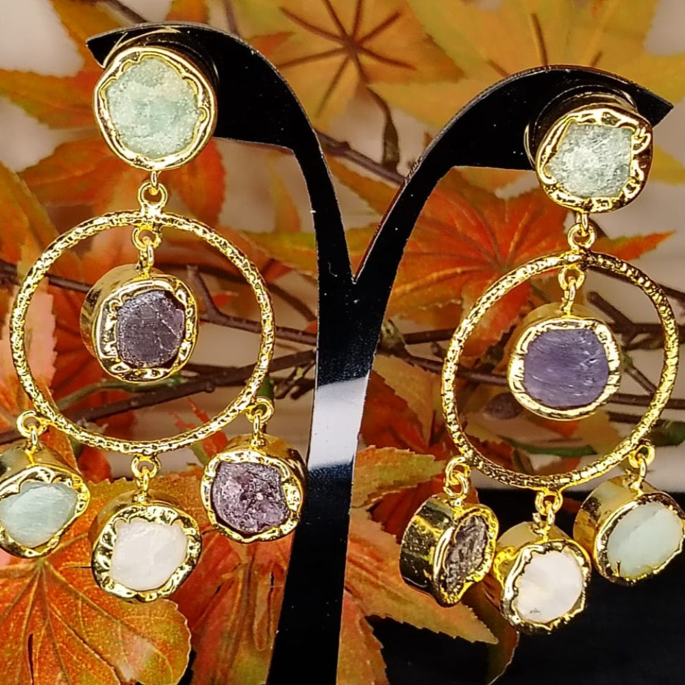 Golden earrings with colorful natural stones on a stand with autumn leaves in the background