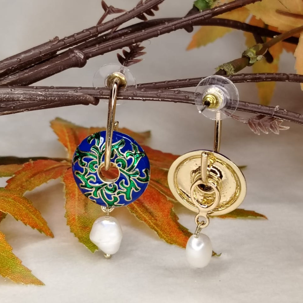 Gold earrings with blue and green circular design and pearl drops on a branch with leaves.