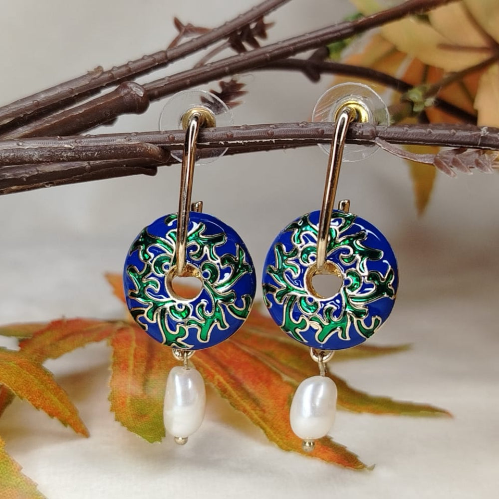 Decorative earrings with blue floral design and pearl beads on a branch with leaves.
