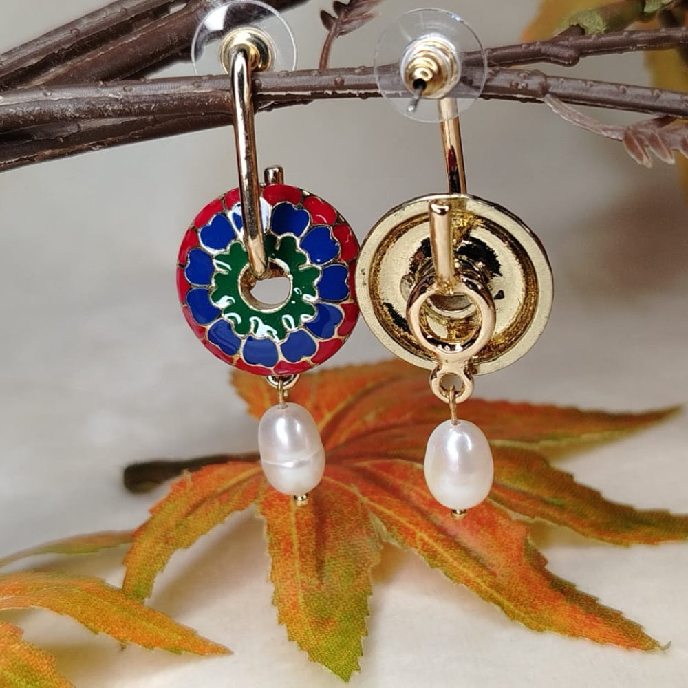 Gold earrings with colorful circular design and pearl drops on a branch with leaves.